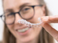 smiling woman using clear plastic removable braces aligner or whitening tray. dental orthodontic care